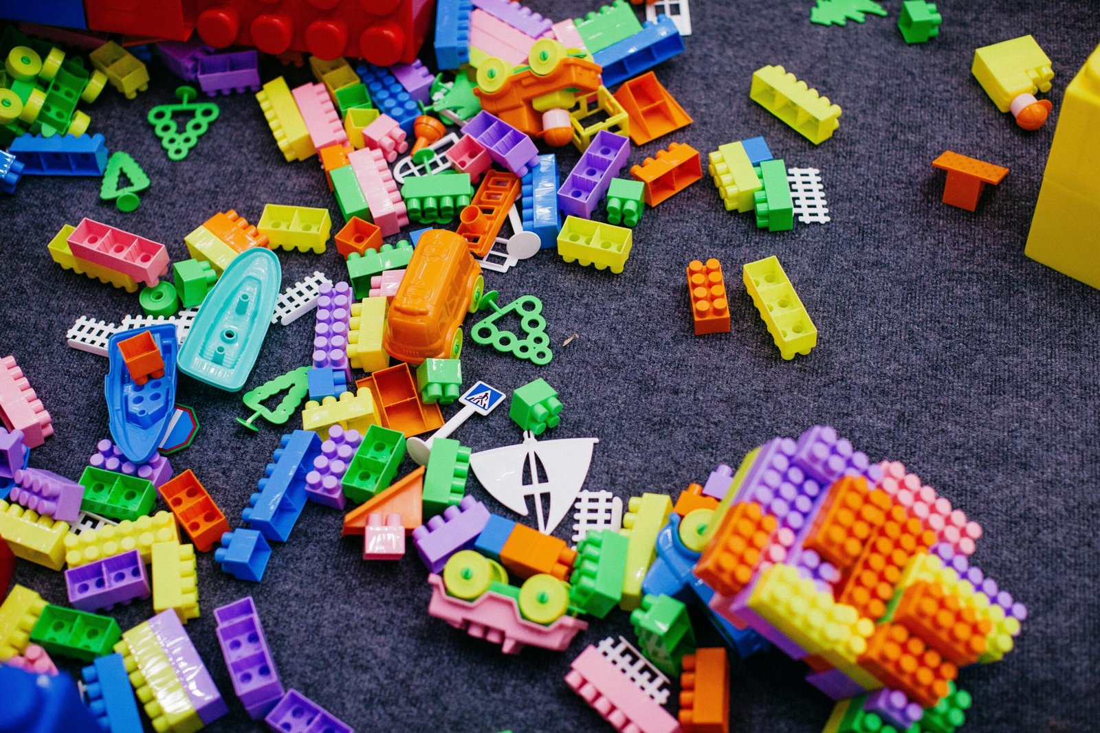 “Colorful plastic building blocks scattered on a dark carpet, with some connected into small toy structures including boats and wheels.”