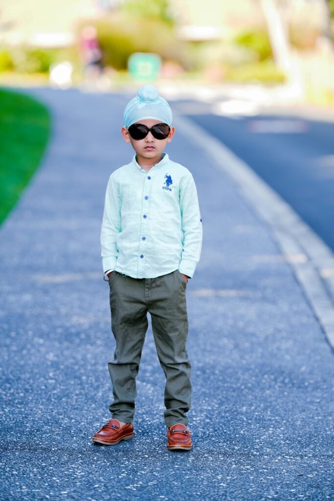 A fashionable child with sunglasses stands confidently on a city sidewalk.