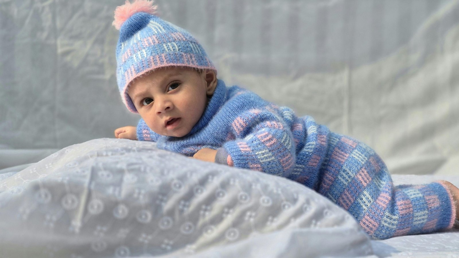 Charming baby in blue and pink knit outfit, laying comfortably indoors.