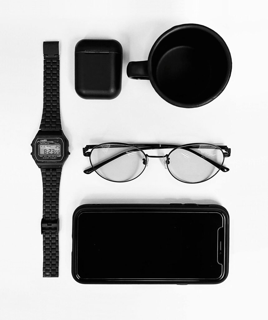 A stylish flat lay featuring a watch, smartphone, eyeglasses, cup, and earbuds on a white background.