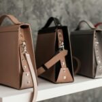 Luxury leather handbags displayed on a white shelf, showcasing minimalistic design and various colors.